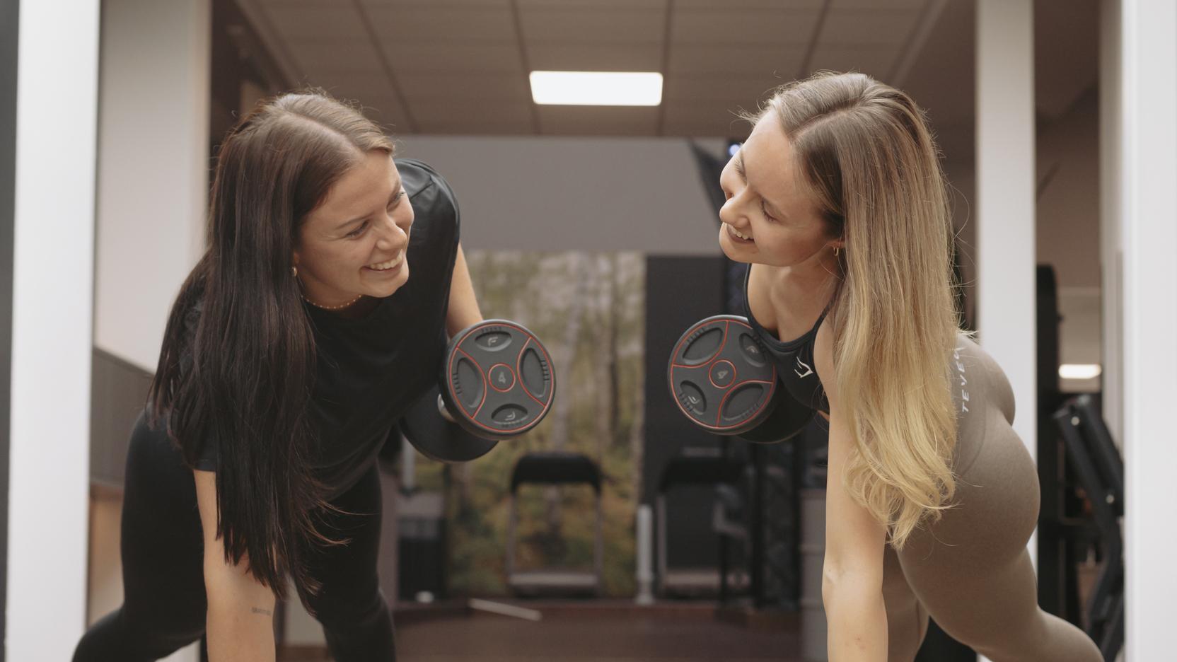 Zwei Frauen führen eine Plank-Übung mit Hanteln in einem modernen Fitnessstudio durch.