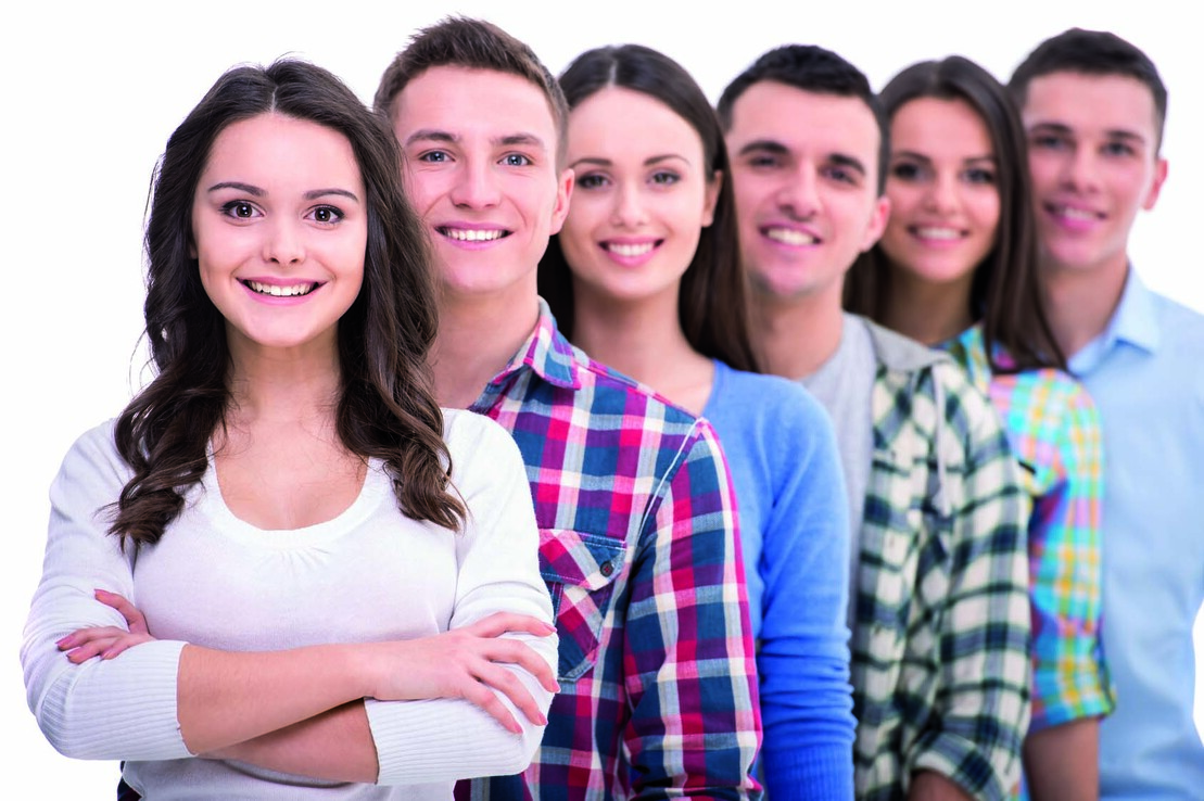 Sechse junge Menschen l&auml;cheln in einer Reihe, vorne steht eine Frau mit langen Haaren und verschr&auml;nkten Armen.