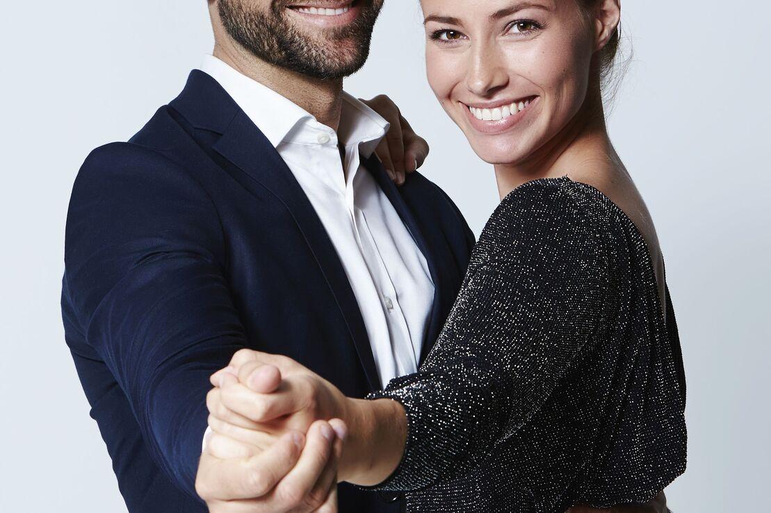 Ein Paar tanzt l&auml;chelnd miteinander, der Mann tr&auml;gt einen Anzug, die Frau ein glitzerndes Kleid.