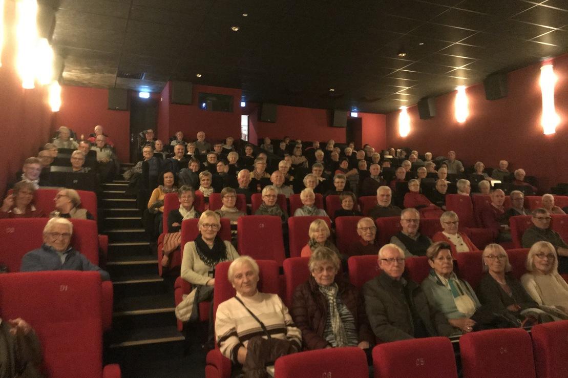 Publikum in einem Kino sitzt in roten Sesseln und blickt auf die Leinwand, zahlreiche Menschen besetzen die Reihen.