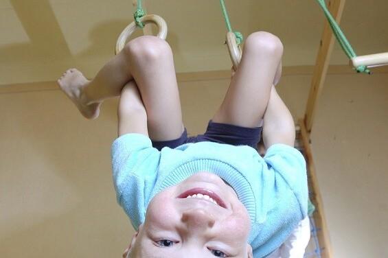 Ein Junge h&auml;ngt an Ringen in einem Spielraum und l&auml;chelt, im Hintergrund ist ein weiteres Kind sichtbar.