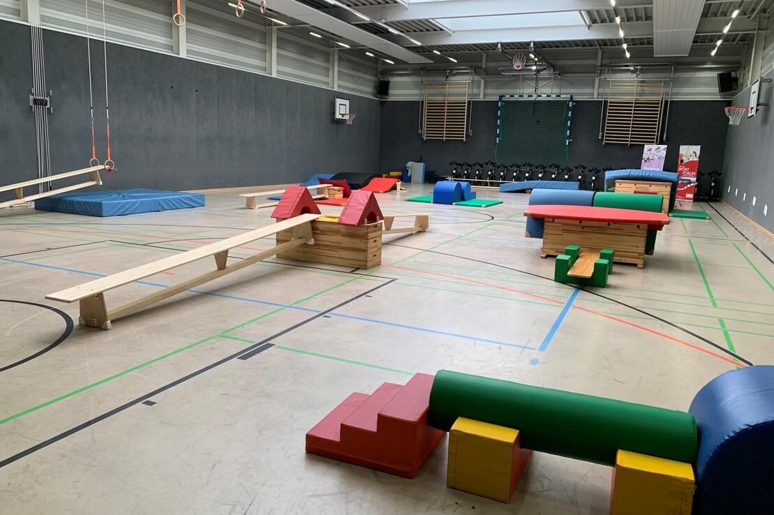 Turnhalle mit verschiedenen Bewegungsger&auml;ten aus Holz und buntem Schaumstoff, verstreut auf dem Boden.