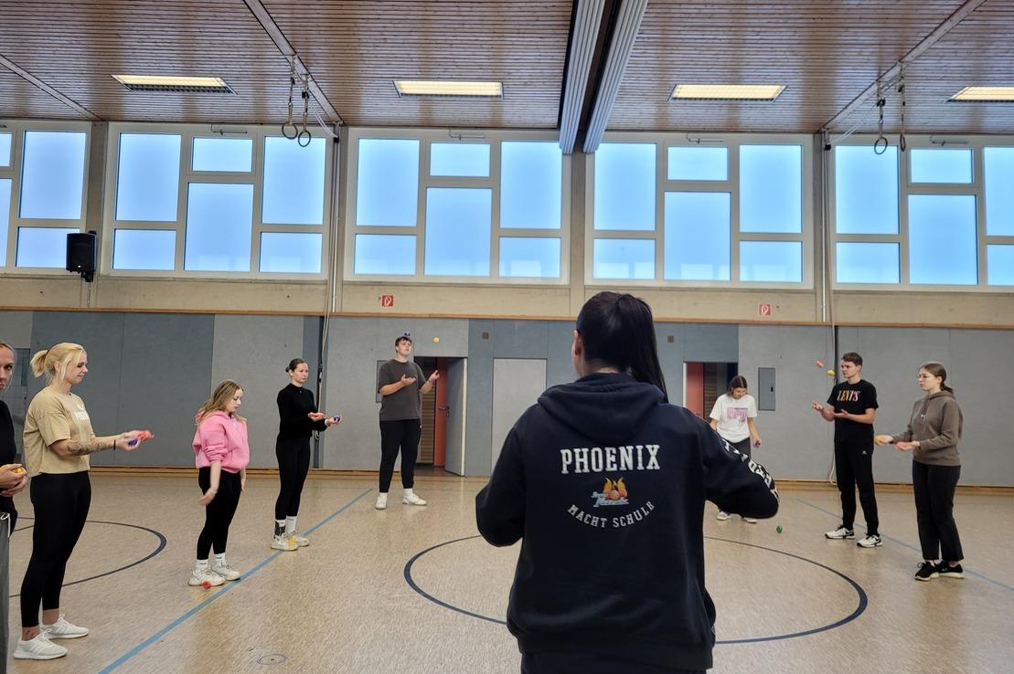 Gruppe von trainierenden Personen in einem Raum, angeleitet von einer Trainerin mit &bdquo;PHOENIX&ldquo;-Hoodie.