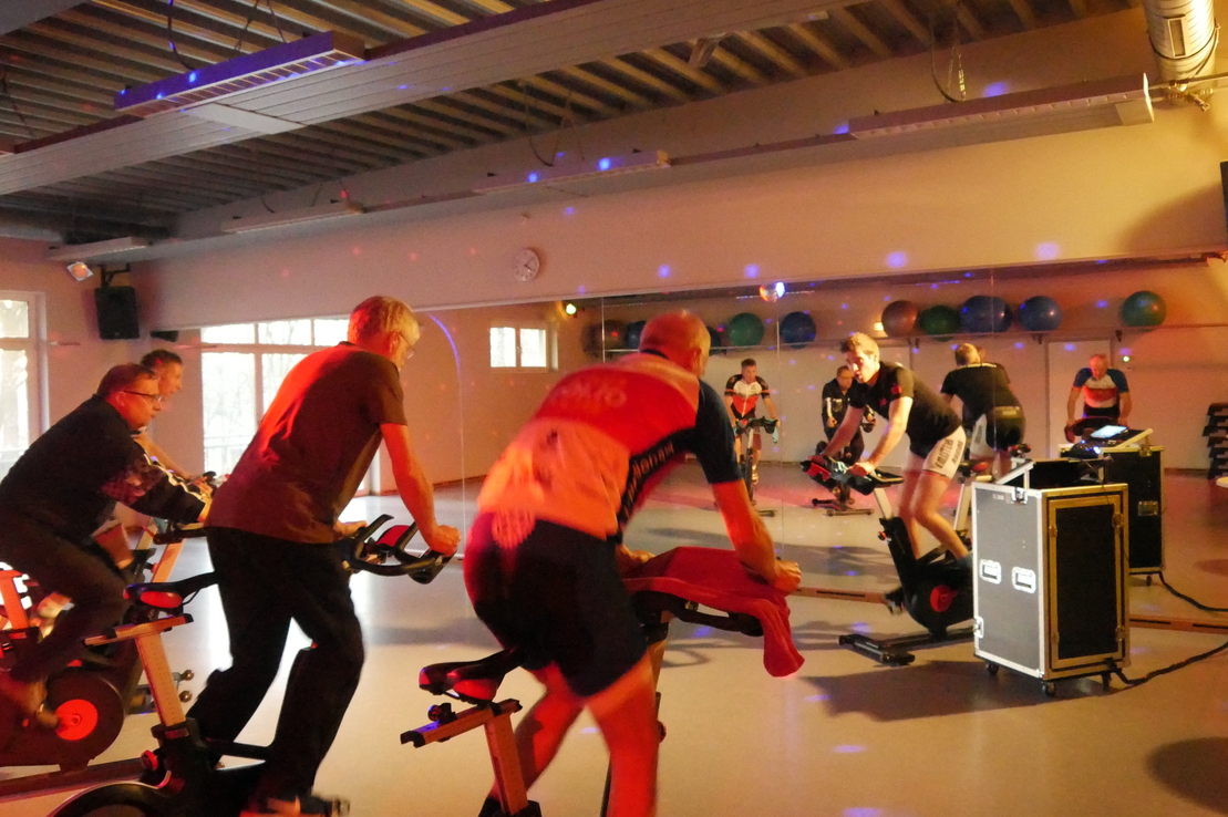 Gruppenausdauertraining mit mehreren Personen auf Spinning-Bikes in einem beleuchteten Fitnessraum.