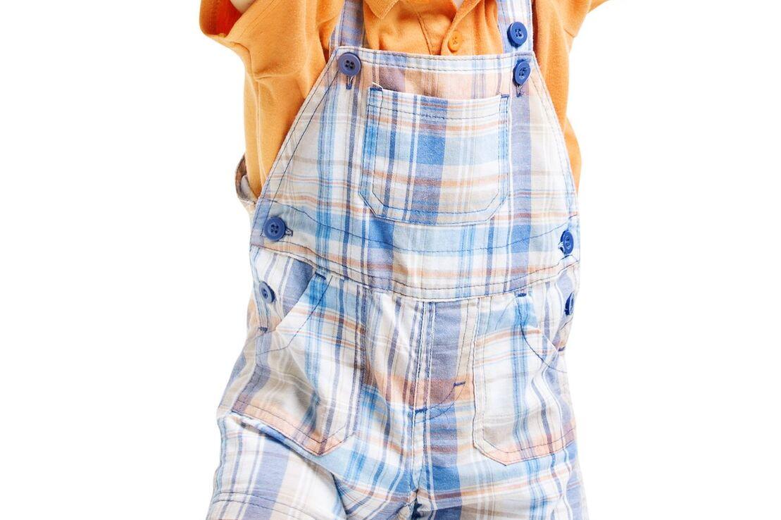 Kleines Kind in gestreifter Latzhose und orangefarbenem T-Shirt, das fr&ouml;hlich mit erhobenen H&auml;nden steht.