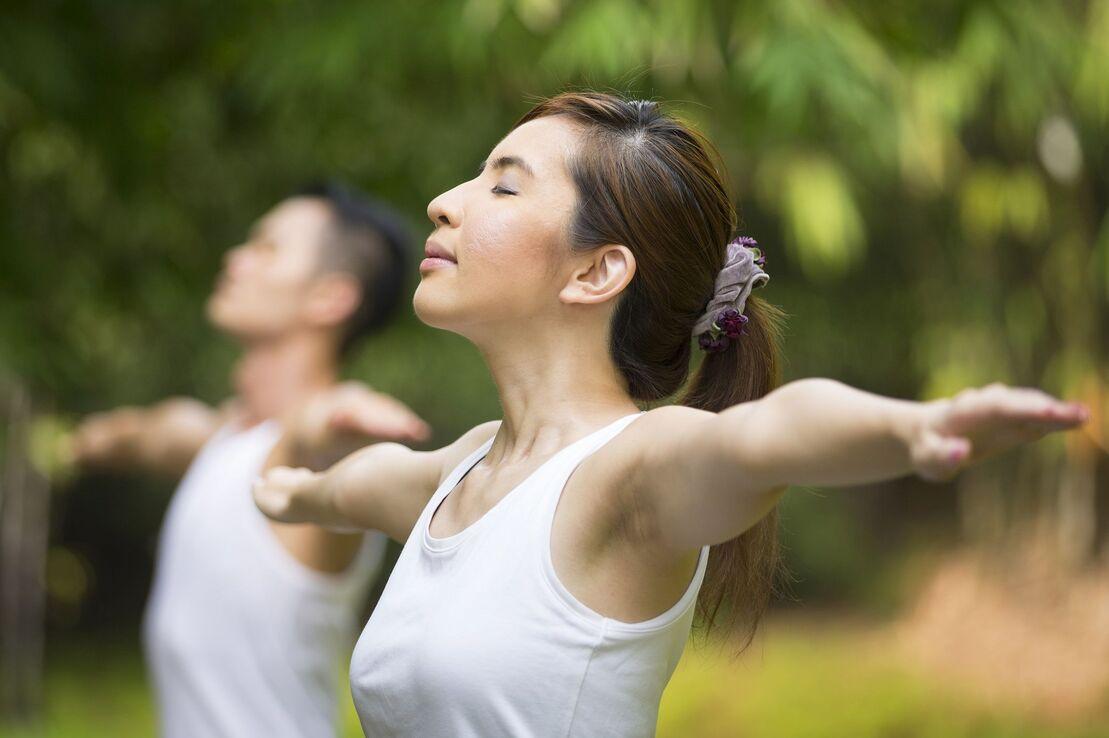 Zwei Personen in Sportkleidung praktizieren Yoga im Freien, mit geschlossenen Augen und ausgestreckten Armen.