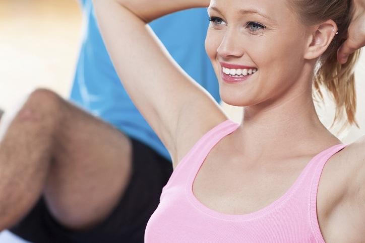 Zwei Personen machen Sit-ups auf Gymnastikmatten in einem Fitnessraum, die Frau in einem pinken Top, der Mann in einem blauen Shirt.