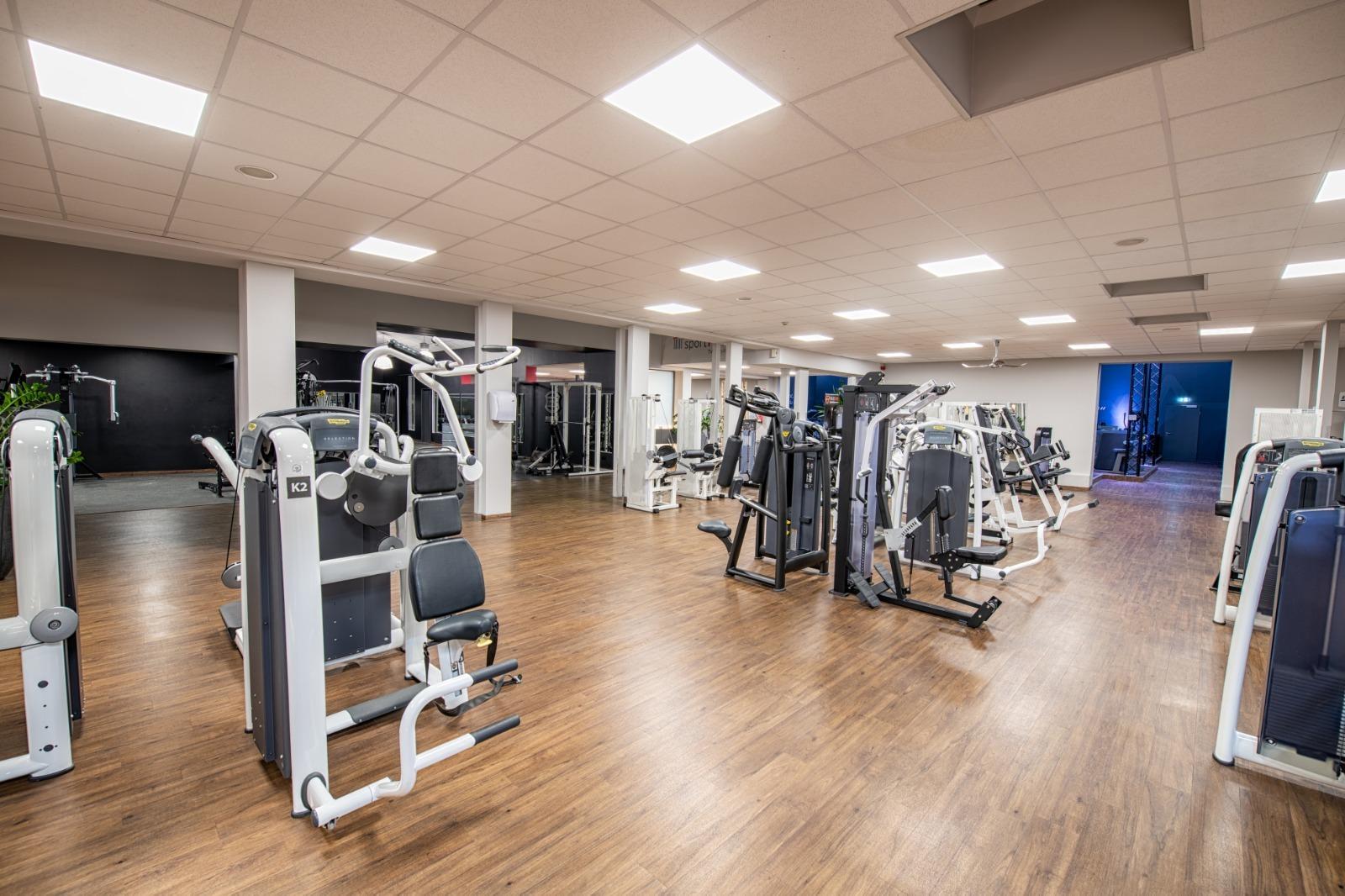 Kardioger&auml;te und Kraftstationen in einem modernen Fitnessstudio mit Holzfu&szlig;boden und hellem Licht.