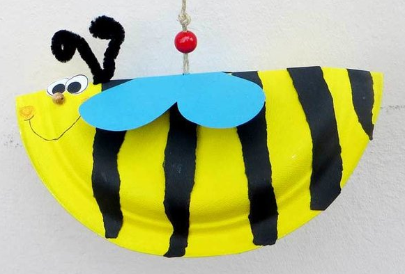 Pappfigur einer Biene mit gelb-schwarzen Streifen und blauen Fl&uuml;geln, aufgeh&auml;ngt mit einer roten Perle.