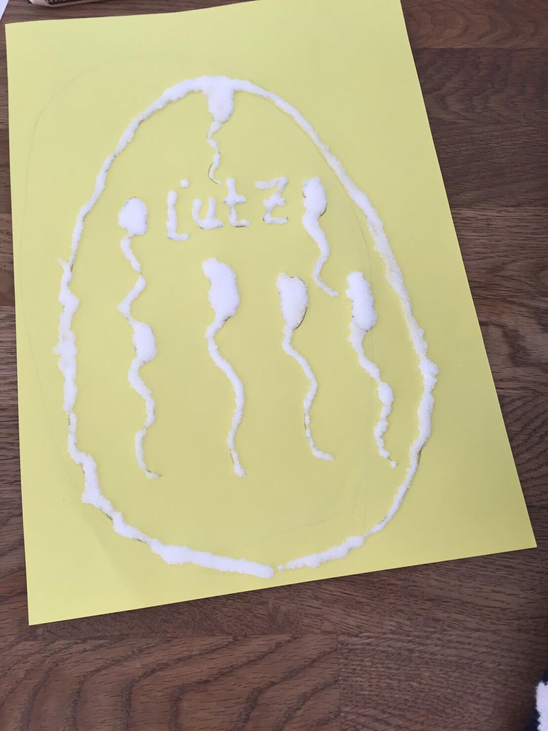 Gelbe Papieroberfl&auml;che mit wei&szlig;em, k&ouml;rnigem Material, das in Form von Spermien und dem Wort &bdquo;L&uuml;tz&ldquo; gestaltet ist.