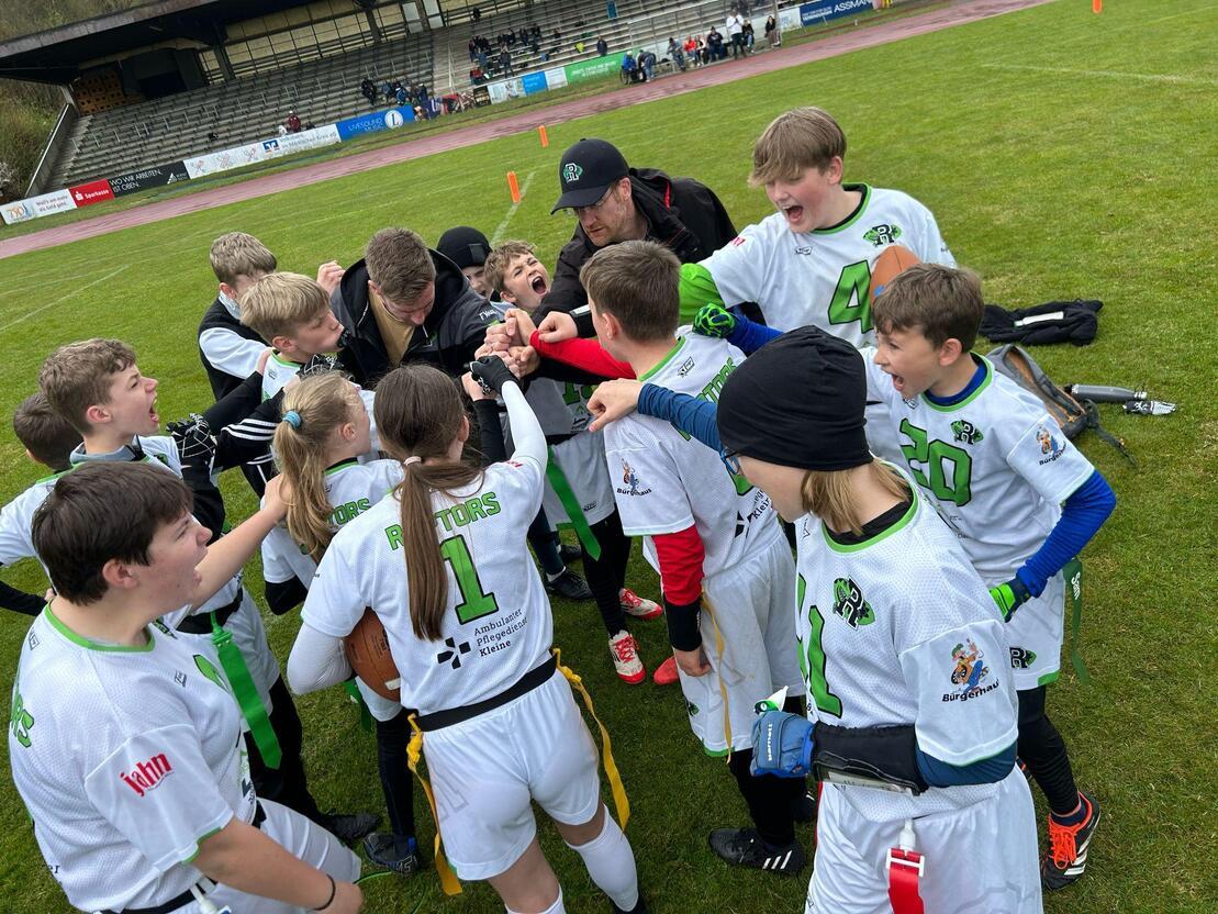 Gruppe junger Sportler in wei&szlig;en Trikots versammelt sich auf dem Rasen f&uuml;r eine Teamansprache vor einem Spiel.