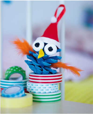 Bunte Weihnachtsdekoration: Ein Bastelvogel aus einer Tannenzapfen, mit rotem Hut und orangefarbenen Federn, sitzt auf bunten Rollen.