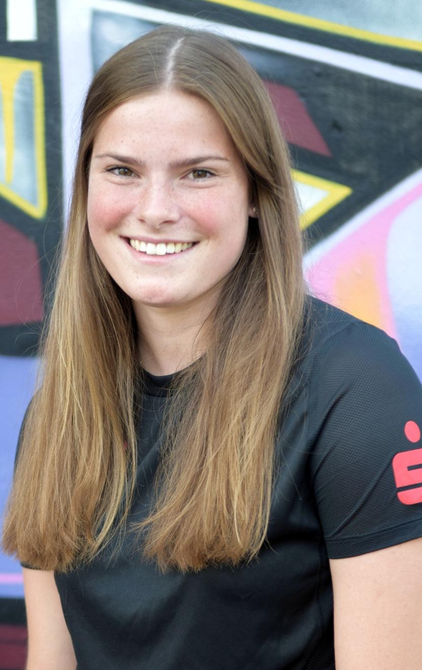 L&auml;chelnde junge Frau mit langen Haaren in schwarzem Shirt vor buntem Graffiti-Hintergrund.