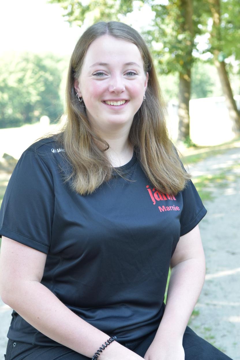 Portr&auml;t einer l&auml;chelnden Frau mit langen, lockigen Haaren in einem schwarzen Shirt, sitzend im Freien.