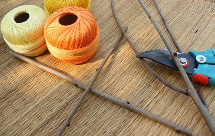 Zwei Spulen aus buntem Garn und eine Gartenschere liegen neben mehreren Zweigen auf einem geflochtenen Untergrund.