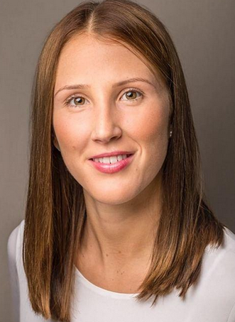 Portr&auml;t einer l&auml;chelnden Frau mit langen, braunen Haaren, die einen wei&szlig;en Oberteil tr&auml;gt und vor einem neutralen Hintergrund steht.