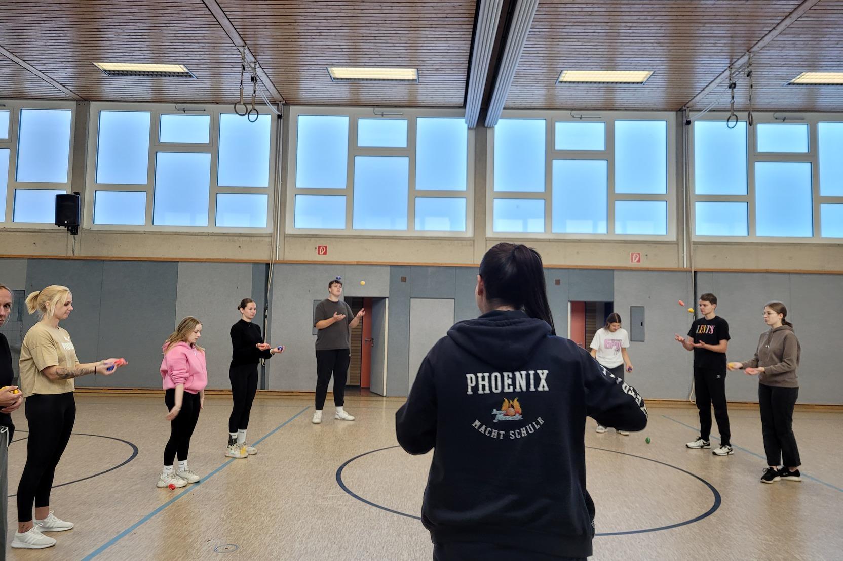 Gruppe von trainierenden Personen in einem Raum, angeleitet von einer Trainerin mit &bdquo;PHOENIX&ldquo;-Hoodie.