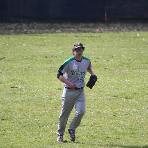 Baseballspieler in Uniform l&auml;uft auf einem Rasenfeld, mit Handschuh in der Hand und einem konzentrierten Blick.