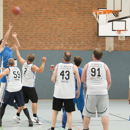 Spieler im Basketballtrikot werfen einen Ball auf den Korb, w&auml;hrend andere Spieler in der N&auml;he stehen.