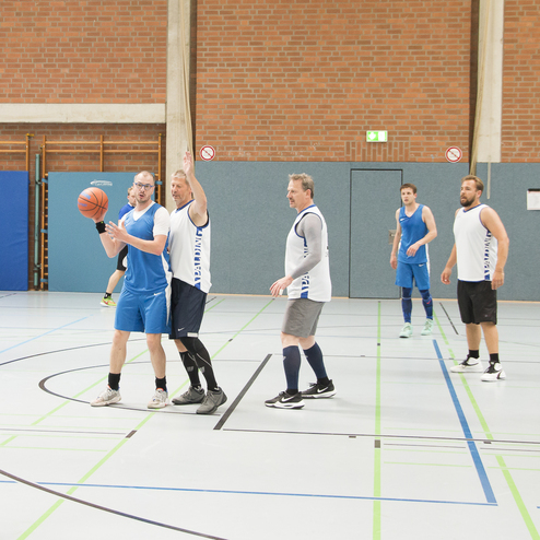 Szenenbild eines Basketballspiels in einer Halle mit Spielern in blauen und wei&szlig;en Trikots.