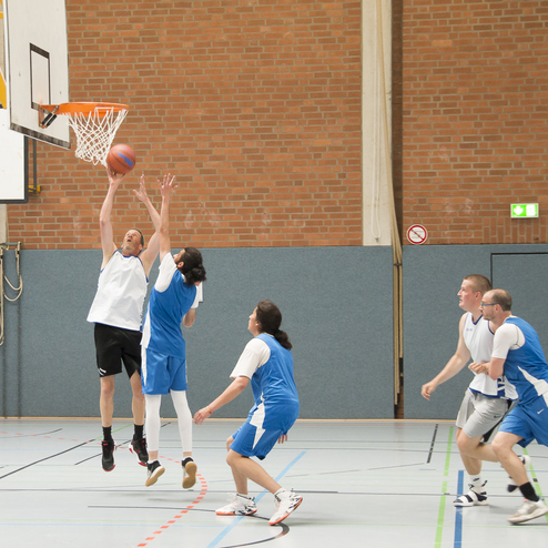 Spieler in blauen Trikots versuchen, einen Basketballwurf gegen einen gegnerischen Spieler im wei&szlig;en Trikot zu verteidigen.
