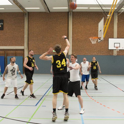 Spielszene im Basketball: Ein Spieler wirft einen Ball aufs Korb, w&auml;hrend andere Spieler in der Halle agieren.