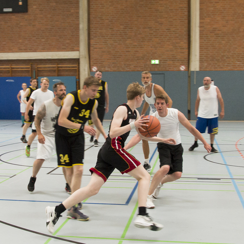 Gruppenspiel auf einem Basketballfeld mit mehreren Spielern in schwarzen und wei&szlig;en Trikots und einem Basketball.