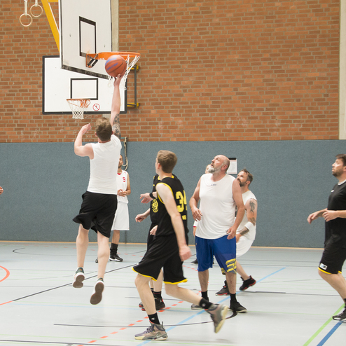 Spieler springt zum Korb, um einen Basketball zu werfen, w&auml;hrend andere Spieler in der Halle zuschauen.