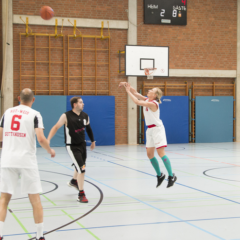 Basketballspiel, ein Spieler in wei&szlig; wirft den Ball, andere Spieler in schwarzen Trikots stehen bereit.