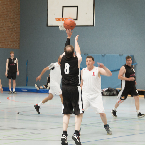 Spieler in schwarzer Trikots werfen einen Basketball w&auml;hrend eines Spiels gegen eine Mannschaft in wei&szlig;en Trikots in einer Halle.