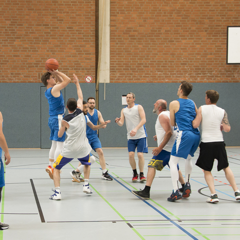 Basketballspieler werfen den Ball zum Korb, w&auml;hrend mehrere Spieler in blauen und wei&szlig;en Trikots verteidigen.