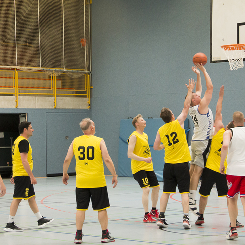 Spielszene mit sieben Basketballspielern in gelben und schwarzen Trikots, w&auml;hrend ein Spieler einen Korbwurf ausf&uuml;hrt.