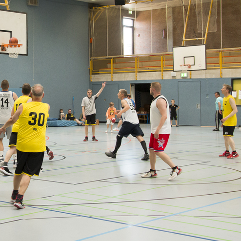 F&uuml;nf Spieler in gelben und wei&szlig;en Trikots werfen den Basketball in einem Hallensportspiel.
