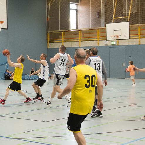 Zwei Basketballmannschaften stehen in einem Spiel auf dem Court, ein Spieler wirft den Ball in Richtung Korb.