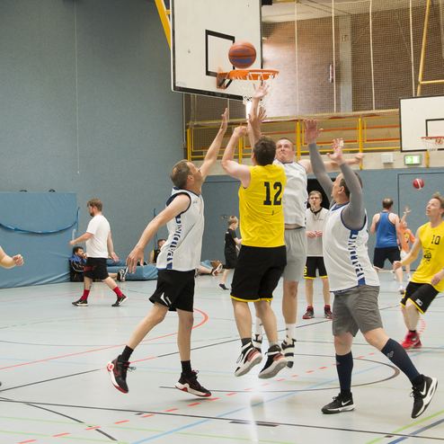 Basketballspiel in einer Halle mit Spielern in gelben und wei&szlig;en Trikots, die den Ball in die Luft werfen.