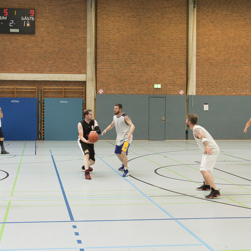 Gameplay in einer Basketballhalle: Zwei Teams k&auml;mpfen um den Ball, Punkte stehen bei 5:9. Spieler mit Schwarz und Wei&szlig; in Aktion.