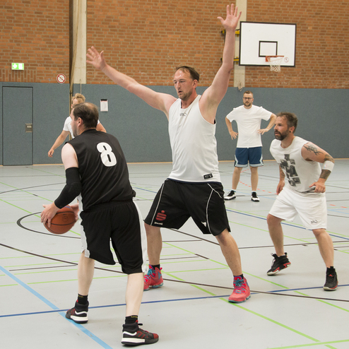 Basketballspiel in einer Halle mit Spielern in Aktion, einer verteidigt einen Angreifer mit Ball.