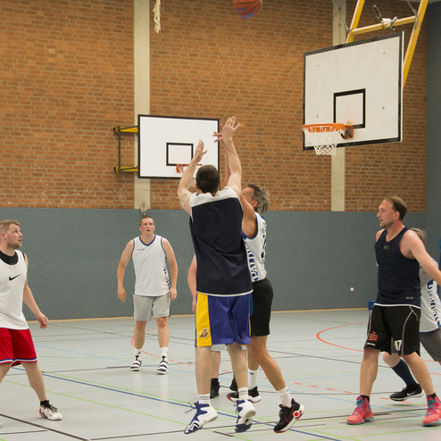 Spieler springen zum Korb, w&auml;hrend ein Basketball im Luftwurf ist; gemeinsame Aktionen auf einem Sportfeld.