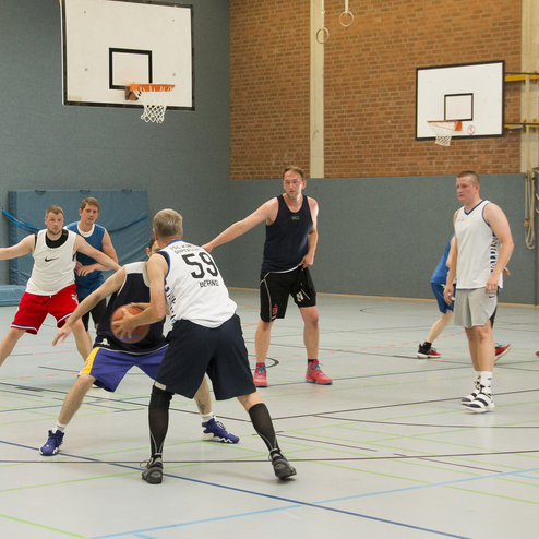 Zwei Spieler dribbeln den Ball w&auml;hrend eines Basketballspiels in einer Sporthalle, umgeben von weiteren Spielern.