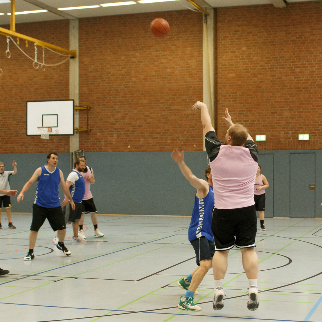 Szenen eines Basketballspiels in einer Sporthalle, Spieler werfen den Ball in Richtung Korb.