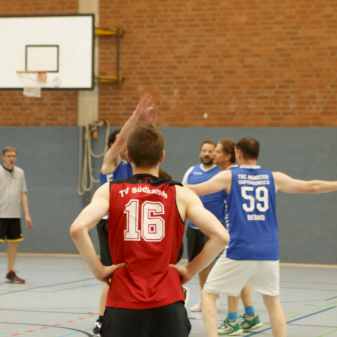 Spielszene in einer Halle mit Spielern in blauen und roten Trikots w&auml;hrend eines Basketballspiels.