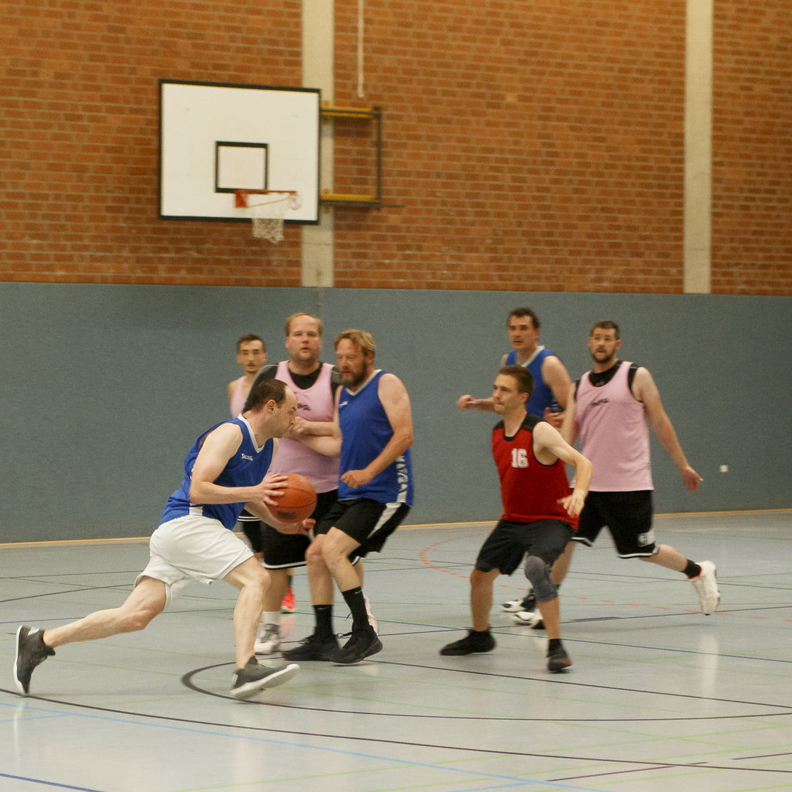 Eine Gruppe von Spielern in Basketballtrikots spielt ein intensives Spiel auf einem Hallenboden.