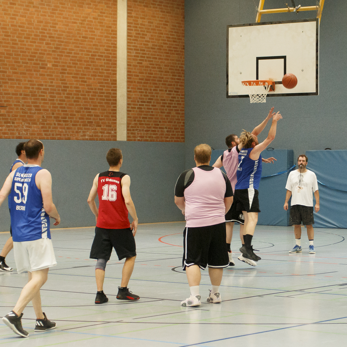 Mehrere Basketballspieler in einem Sporthallenumfeld sprengen den Ball beim Wurf in den Korb.