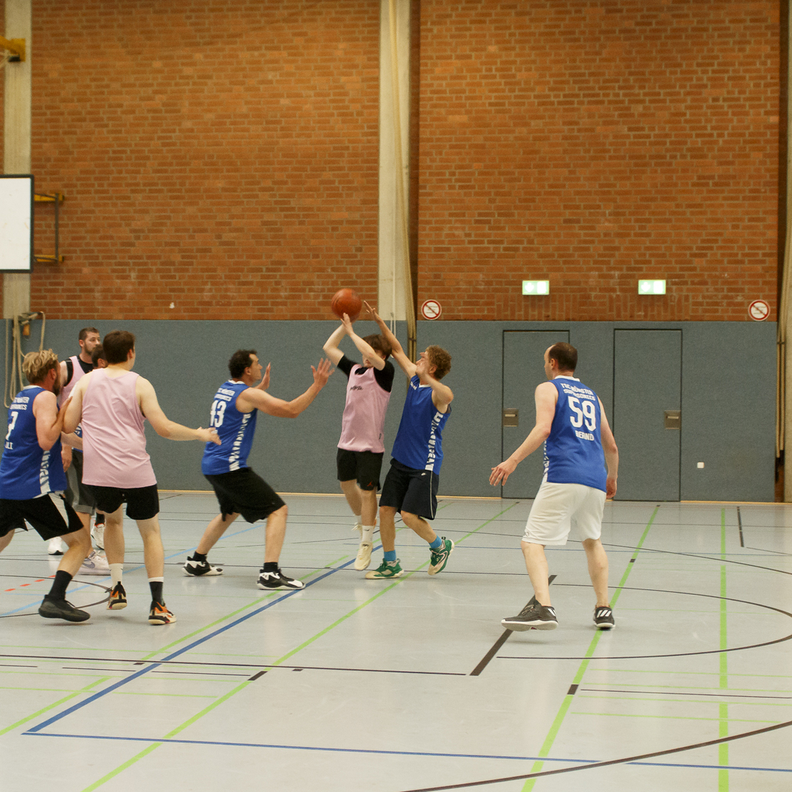 Zwei Teams spielen Basketball in einer Halle, w&auml;hrend ein Spieler einen Wurf versucht.