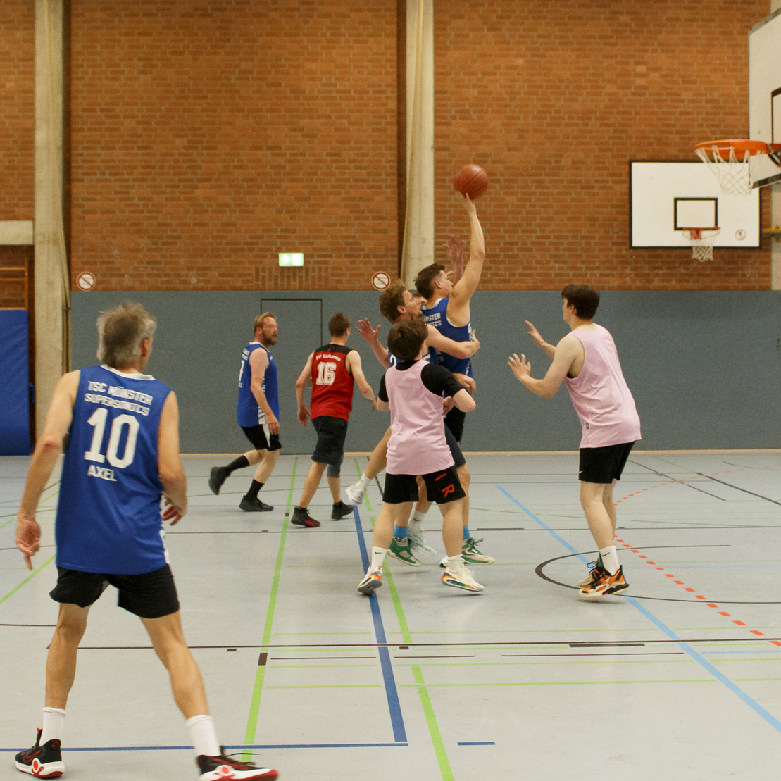 Ein Basketballspieler springt zum Korb, w&auml;hrend andere Spieler auf dem Spielfeld agieren.