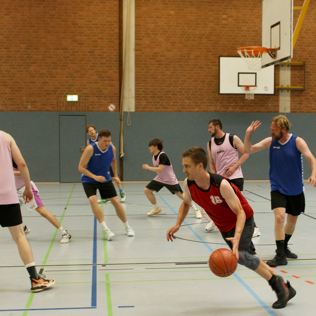 Mehrere Basketballspieler in Aktion auf einem Feld, ein Spieler dribbelt den Ball, andere Spieler in Bewegung.