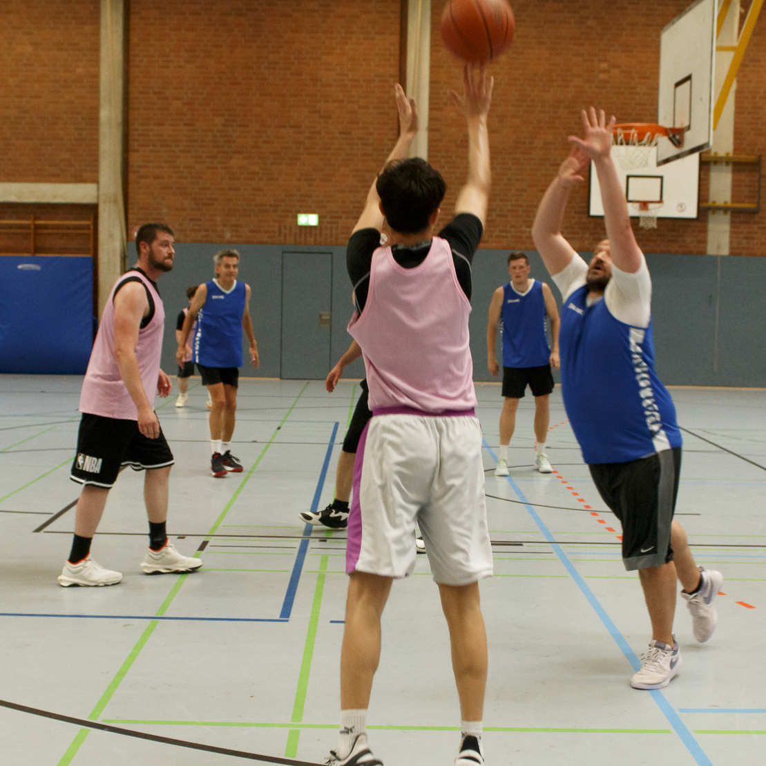 Basketballspiel in der Halle: Spieler im Trikot werfen und versuchen, den Ball zu blocken. Team mit blauen und pinken Trikots.