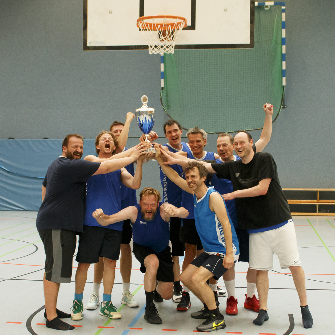 Gruppe von M&auml;nnern in Sportkleidung, die einen Pokal in einer Sporthalle feiern.