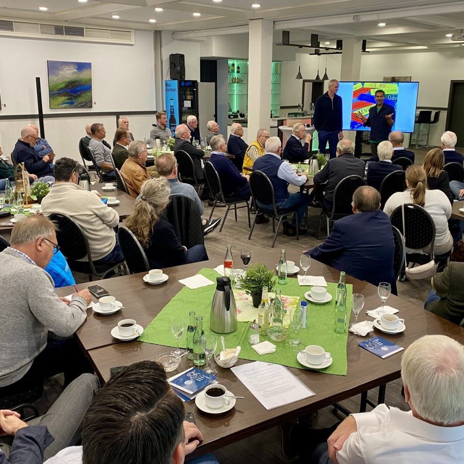 Gruppendiskussion mit Publikum bei einem Event, Pr&auml;sentation auf Bildschirm und Tisch mit Getr&auml;nken und Snacks.
