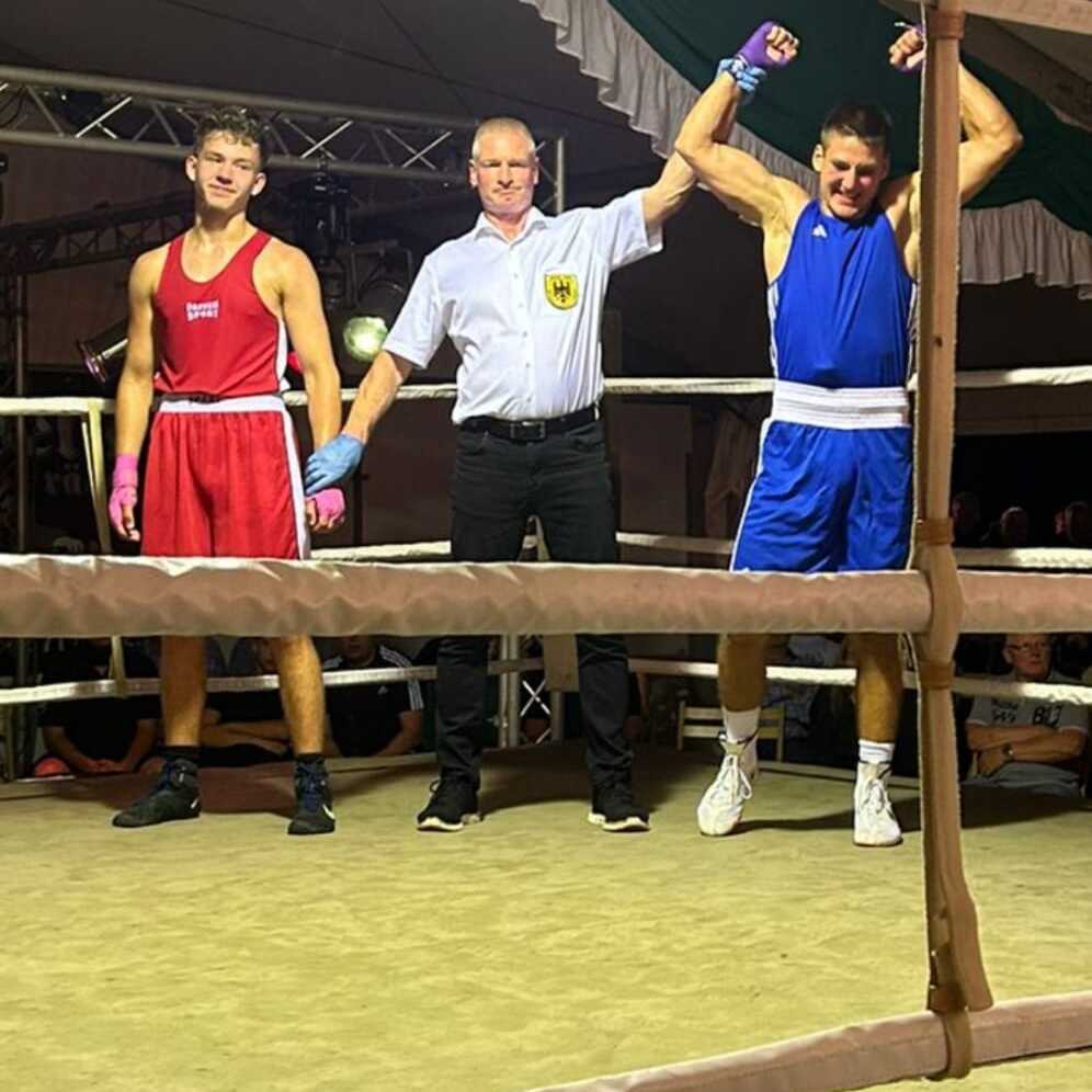 Boxring mit zwei Boxern, einer in roter und einer in blauer Uniform, während ein Schiedsrichter den Sieg verkündet.